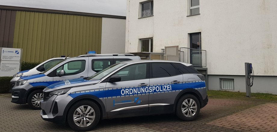 Drei Fahrzeuge der Ordnungspolizei stehen vor einem weißen, mehrstöckigen Gebäude mit grauem Dach an einem bewölkten Tag.