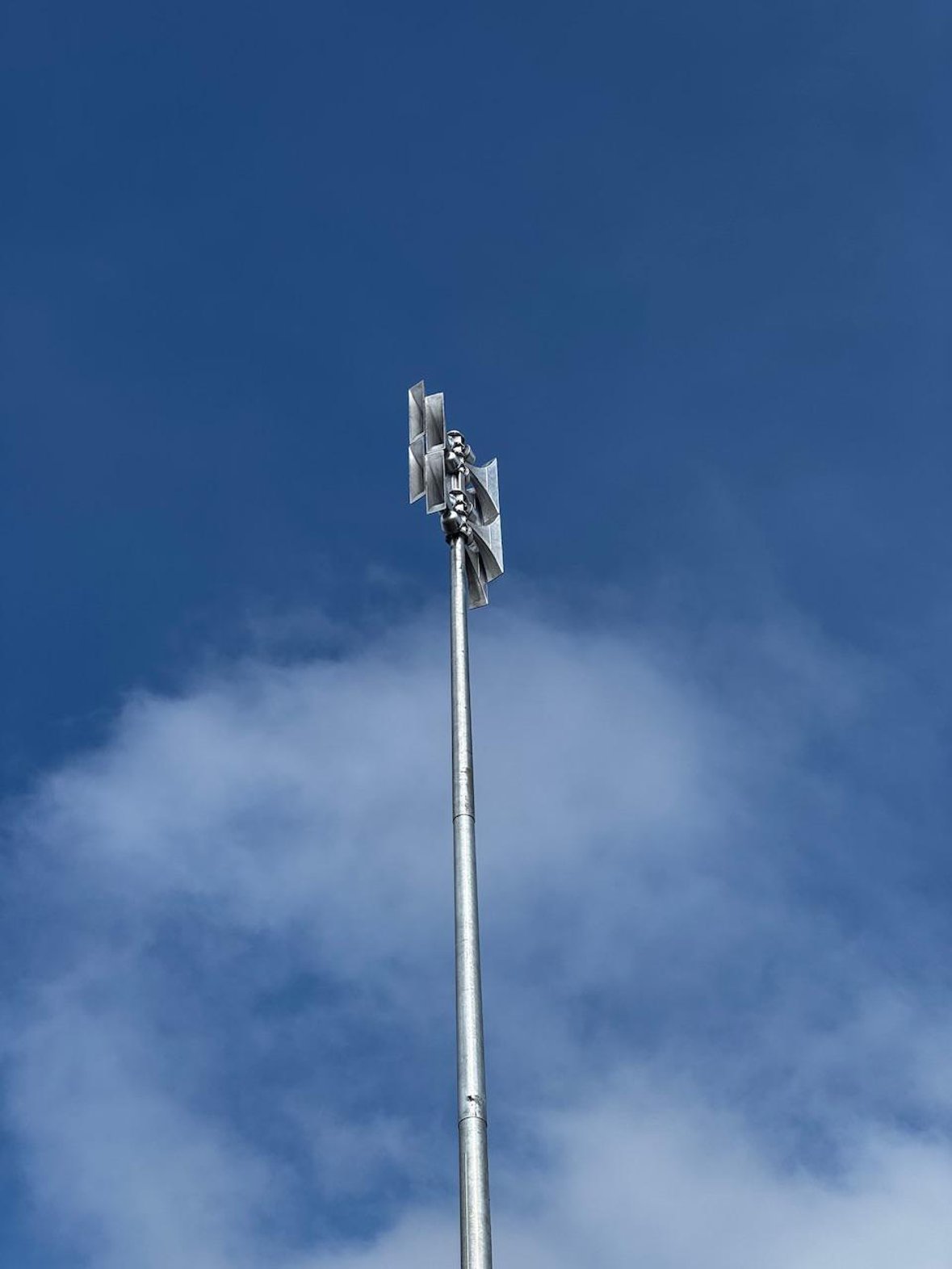 Digitale Sirene auf einem hohen Metallmast vor blauem Himmel mit vereinzelten Wolken.