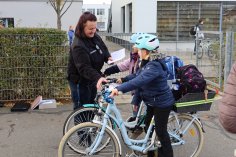Eine Ordnungspolizistin prüft mit Kindern auf Fahrrädern den Fahrradführerschein auf dem Schulhof