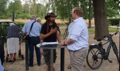 Bürgermeister im Gespräch mit Bürger Bürgermeister im Gespräch mit Bürgern vor dem Rathaus in Rollwald, umgeben von Bäumen und Fahrrädern