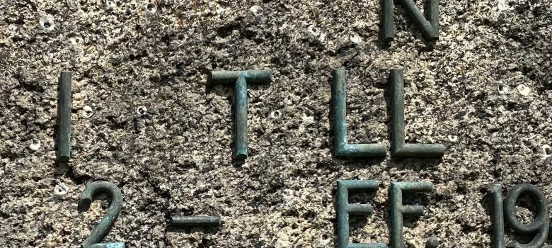 Ahnen- und Familienforschung Bronzebuchstaben und Zahlen auf rauer Steinoberfläche, Teil einer historischen Inschrift zur Ahnen- und Familienforschung