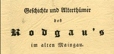 Ein Buchdeckel in alter Schrift mit dem Titel "Geschichte und Alterthümer des Rodgau's im alten Maingau" ist zu sehen. Das Buch hat einen Ledereinband.