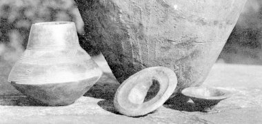 Eine Krug, eine Vase und zwei kleinere, deckelartige Gegenstände sind auf einer Steinplatte aufgestellt.