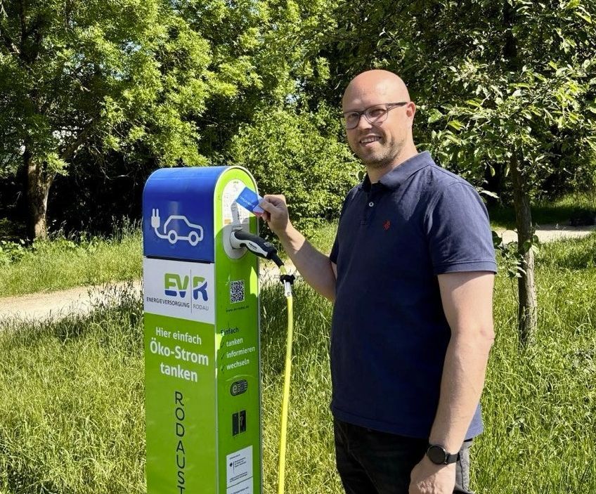 Elektroauto mit rodgaucard laden Mann mit Brille und blauem Poloshirt lädt Elektroauto an grüner Ladesäule im Freien