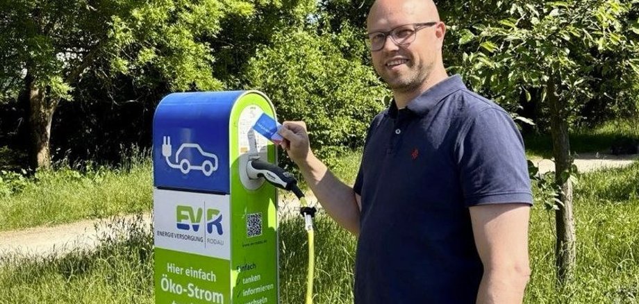Elektroauto mit rodgaucard laden Mann mit Brille und blauem Poloshirt lädt Elektroauto an grüner Ladesäule im Freien
