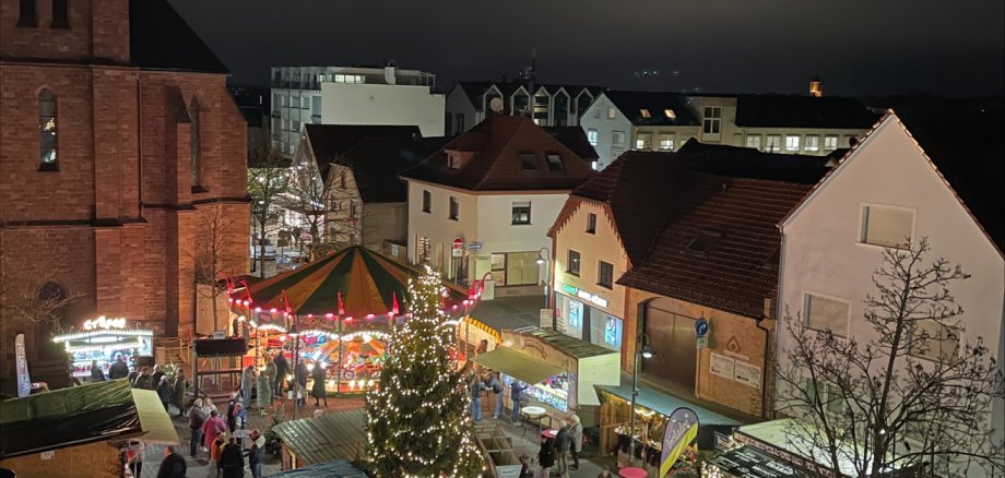 Weihnachtsmarkt in Jügesheim Abendlicher Adventsmarkt auf dem Rathausplatz in Rodgau mit beleuchtetem Weihnachtsbaum, Karussell und Marktständen vor historischen Gebäuden.