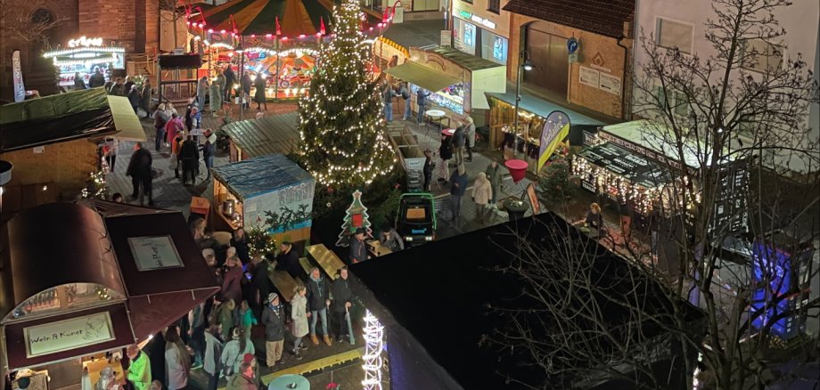 Weihnachtsmarkt in Jügesheim Abendlicher Adventsmarkt auf dem Rathausplatz in Rodgau mit beleuchtetem Weihnachtsbaum, Karussell und Marktständen vor historischen Gebäuden.