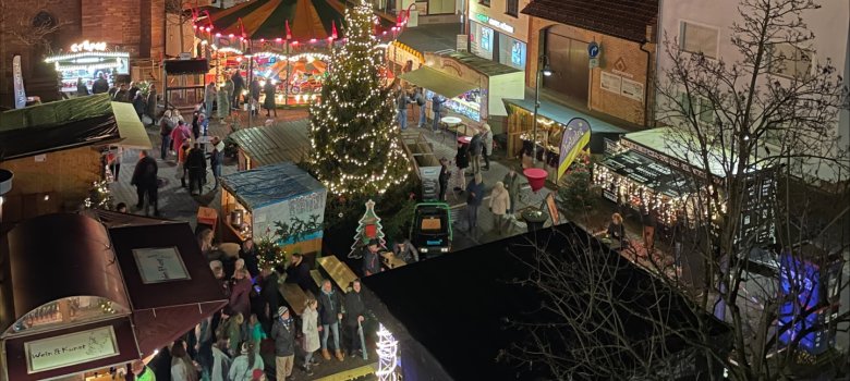 Weihnachtsmarkt in Jügesheim Abendlicher Adventsmarkt auf dem Rathausplatz in Rodgau mit beleuchtetem Weihnachtsbaum, Karussell und Marktständen vor historischen Gebäuden.