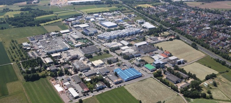 Luftaufnahme des Gewerbegebiets Jügesheim mit verschiedenen Industrie- und Lagerhallen, umgeben von Feldern und angrenzendem Wohngebiet im Hintergrund.