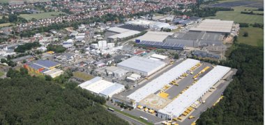 Luftaufnahme des Gewerbegebiets Nieder-Roden-Süd mit großen Lager- und Produktionshallen, umgeben von Wald und angrenzender Wohnbebauung in der Ferne.