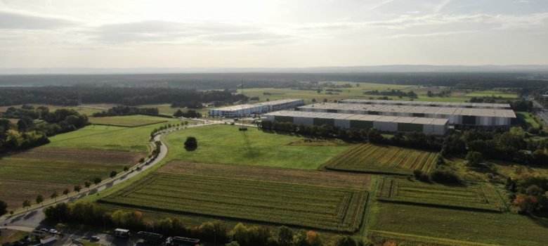 Luftaufnahme des Gewerbegebiets VGP-Park Rodgau mit großen Lagerhallen und umgebenden landwirtschaftlichen Flächen unter bewölktem Himmel.