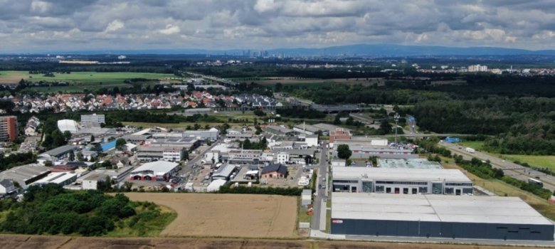 Luftaufnahme des Gewerbegebiets Weiskirchen-Ost mit mehreren Lager- und Industriegebäuden, angrenzenden Feldern und Wohngebieten unter bewölktem Himmel.