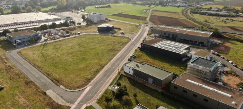 Luftaufnahme des Gewerbegebiets Weiskirchen-West mit mehreren modernen Industrie- und Bürogebäuden, Straßen und angrenzenden Feldern im ländlichen Umfeld.