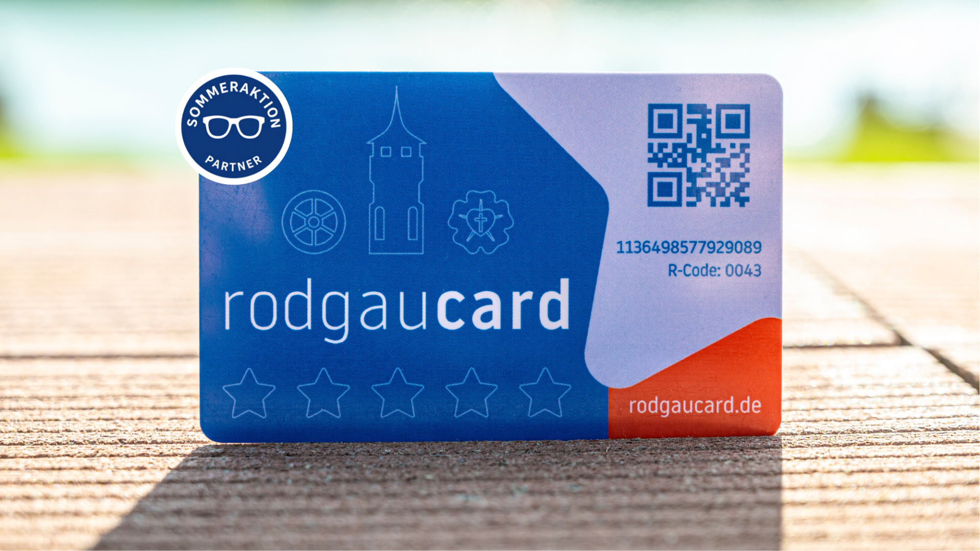 Blaue rodgaucards mit weißem Text, einem QR-Code, Symbolen und dem Schriftzug 'Sommeraktion Partner' auf hölzernem Untergrund